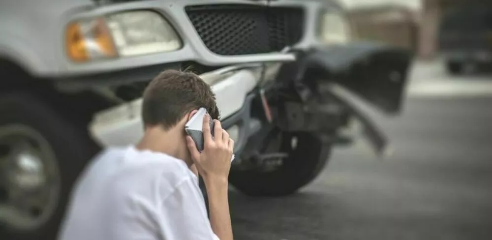 En mann prater i telefonen utenfor en bil. Foto