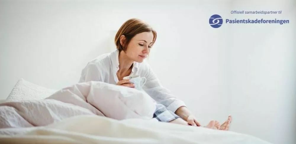 En dame sitter i en seng med en kaffekopp. Foto