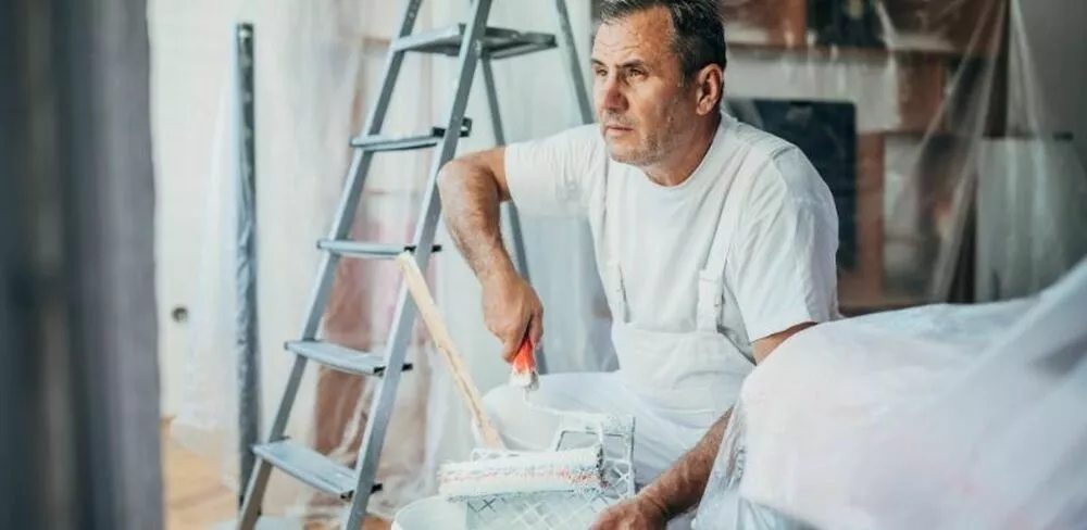 En mann dypper en malekost i maling. Foto